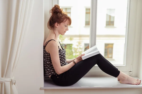 Красивая женщина, читая книгу на подоконнике — стоковое фото